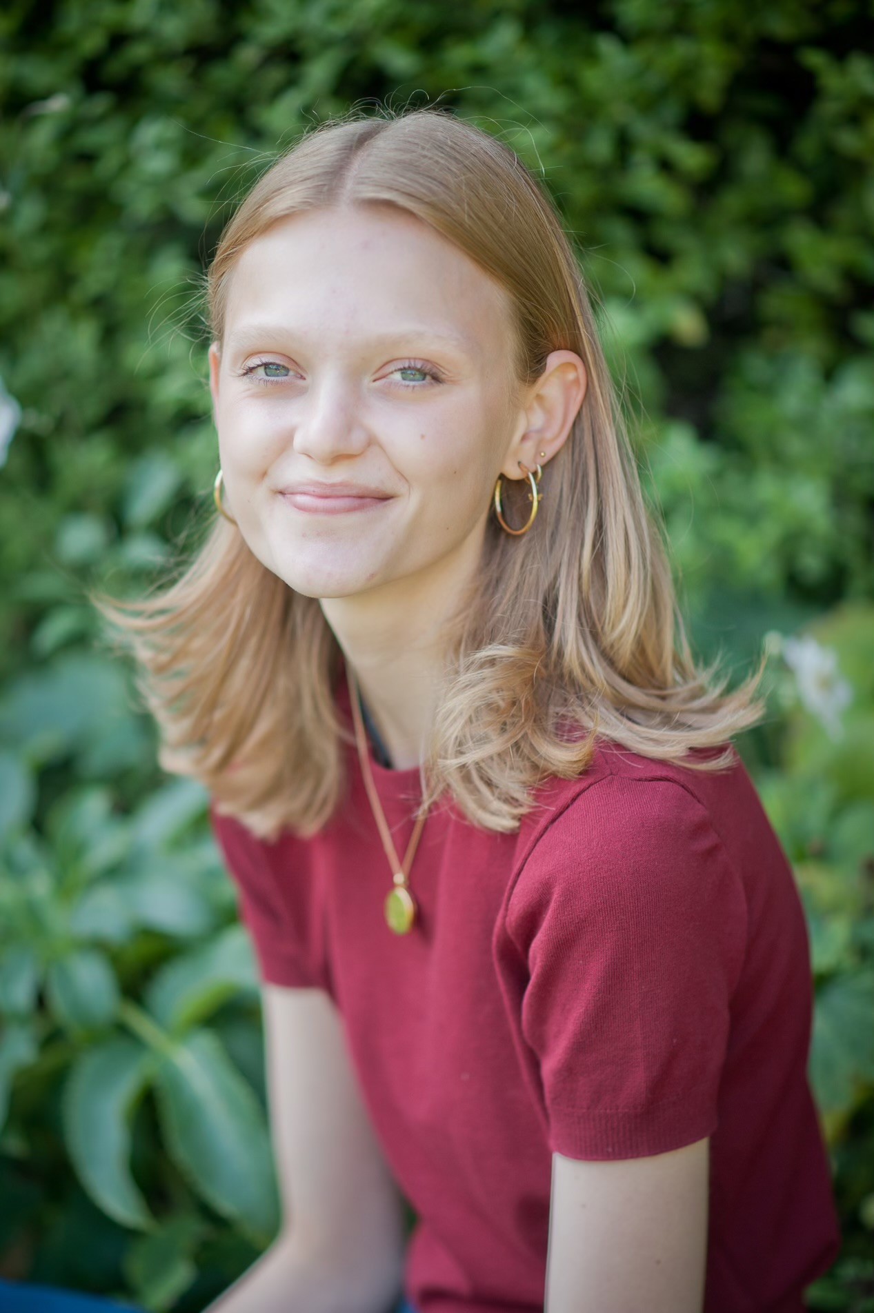 Portrait of Bluebell Craven smiling, in front of a green hedge